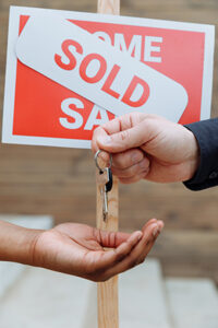 Person handing a set of keys to another hand in front of a Seaside Park real estate sold sign